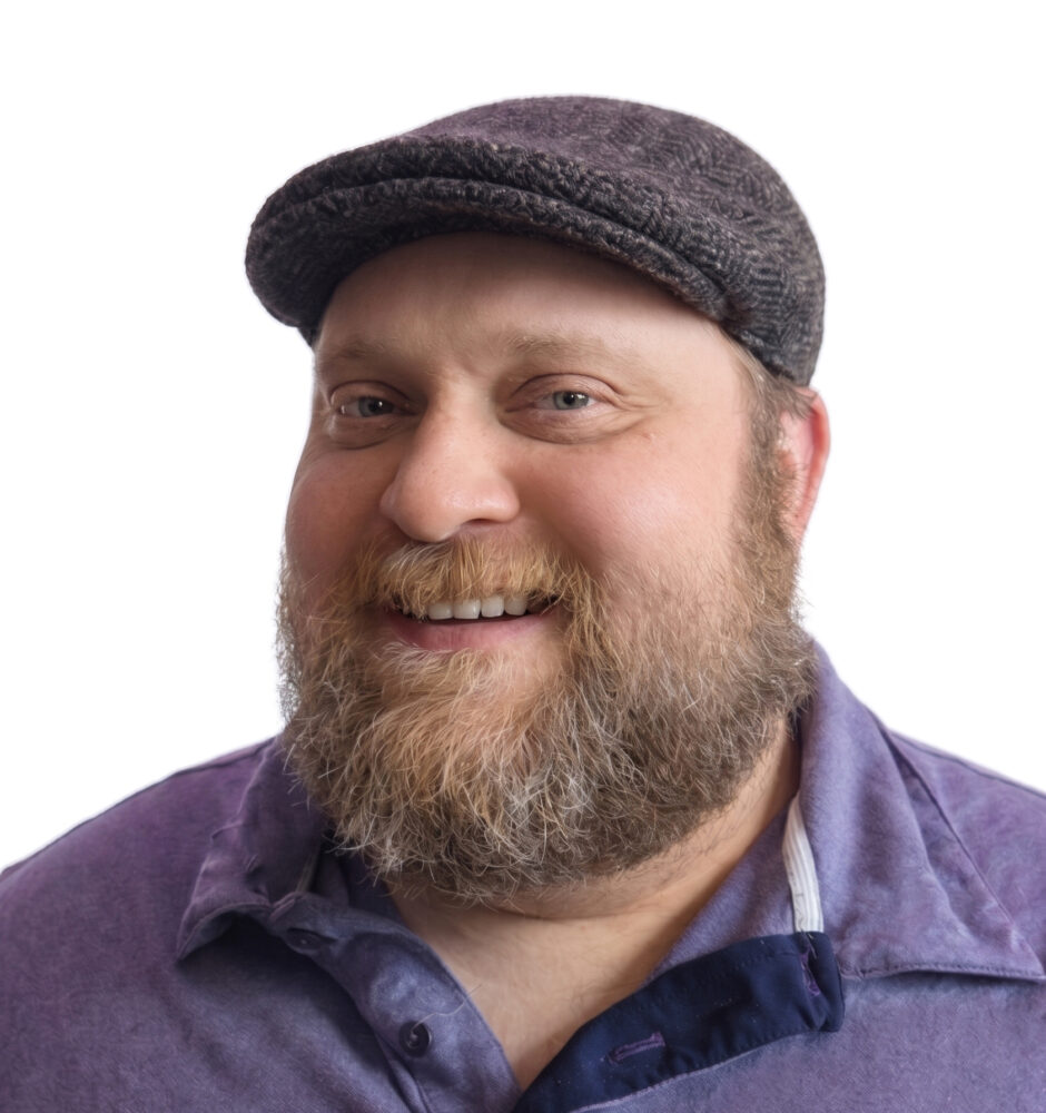 Professional headshot of a smiling man with a beard wearing a dark-colored shirt against a blurred background.
