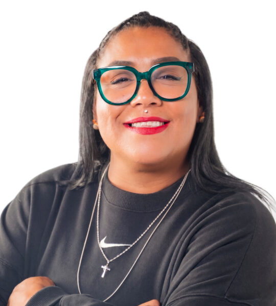 Professional headshot of a smiling woman wearing teal glasses and a black blazer against a white background.