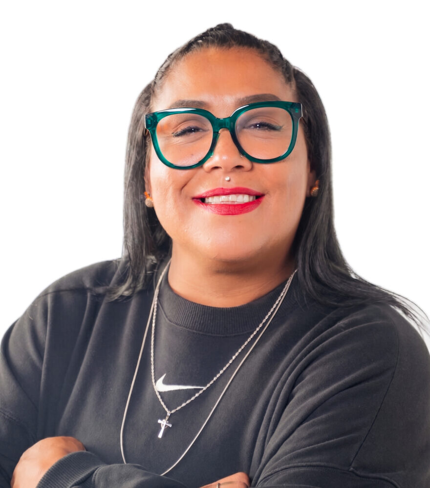 Professional headshot of a smiling woman wearing teal glasses and a black blazer against a white background.