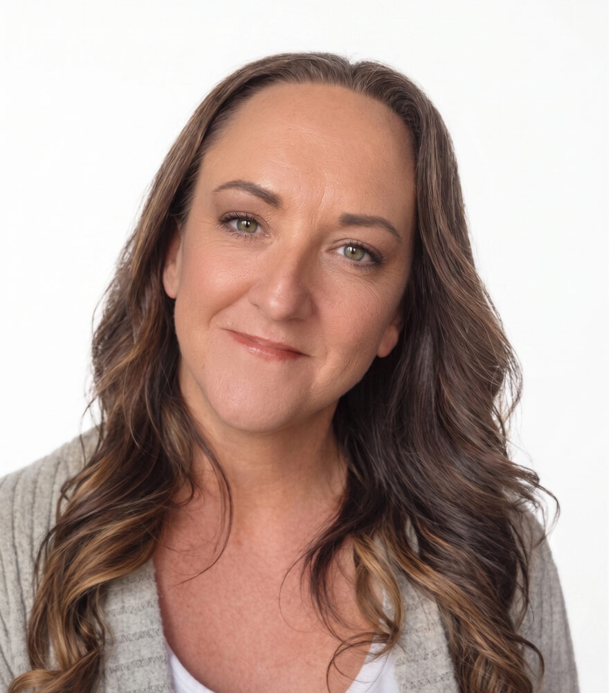 Professional headshot of a woman with brown hair wearing a white top with a light-colored jacket against a blurred background.
