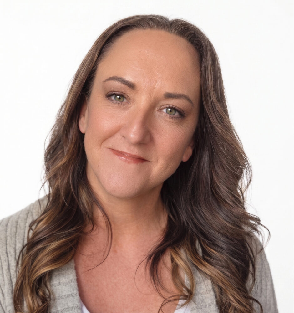 Professional headshot of a woman with brown hair wearing a white top with a light-colored jacket against a blurred background.